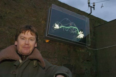 Stephen Healy in front of his animated neon sperm-whale sculpture, installed on the wall of a fishmonger's shop in Peterhead, March 2006. Photograph by Sans fa&ccedil;on.